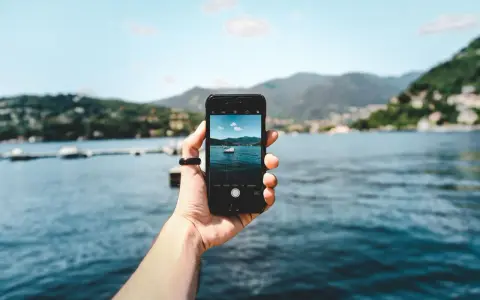 Dłoń trzyma smartfon, na ekranie którego widać zdjęcie jeziora z łódką. To przykład techniki photo stacking, która pozwala uzyskać niezwykłą głębię ostrości.