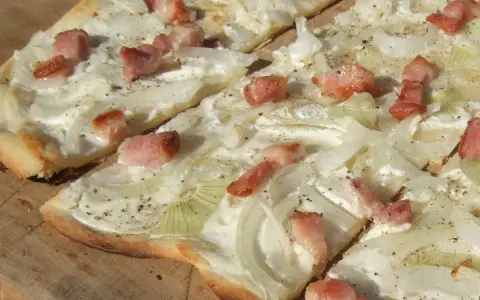 Flammkuchen mit dünnen Zwiebelringen und Speckwürfeln auf Crème fraîche. Ein köstlicher Belag für den knusprigen Teig.
