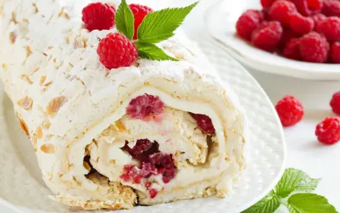 Rolada bezowa z mascarpone i malinami, posypana cukrem pudrem i płatkami migdałów.