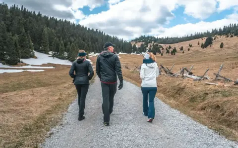 Trzy osoby idące ścieżką w górach. W tle las i pagórkowaty krajobraz.