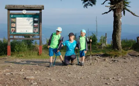 Rodzina na szczycie Baraniej Góry. Dzieci z kijkami trekkingowymi, mama klęczy obok.