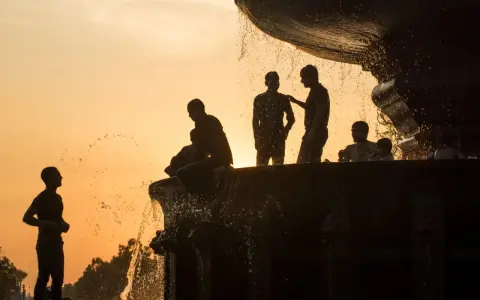 Silhouette fotografia di persone che si rinfrescano in una fontana al tramonto, con l'acqua che scintilla contro il cielo arancione.