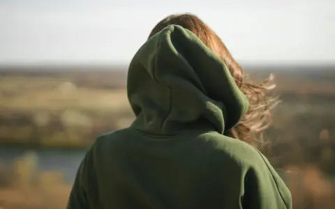 Osoba w zielonej bluzie z kapturem patrzy na krajobraz. Nie wiadomo, ile waży bluza z kapturem, ale wygląda na ciepłą.
