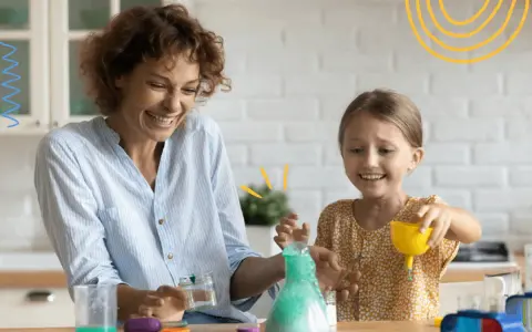 Mama i córka śmieją się, wykonując spektakularne eksperymenty dla dzieci z zieloną pianą w probówce.