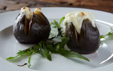 Zwei gefüllte Feigen, die auf einem Teller mit Rucola und Balsamico-Glasur liegen. Ein köstliches Gericht, das zeigt, wie man Feigen grillen kann.