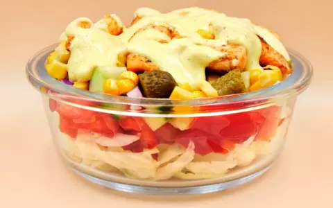 Sałatka gyros w szklanej misce z kurczakiem, kukurydzą, ogórkiem i sosem.