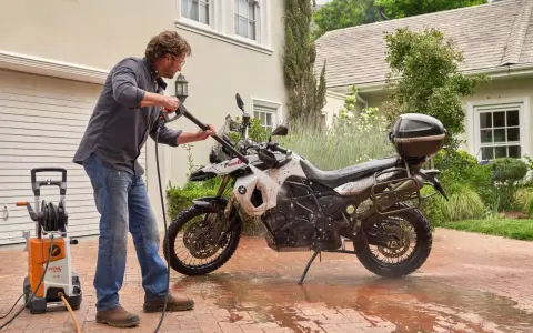 Uomo lava moto a idropulitrice in giardino. Ecco come lavare la moto a casa per mantenerla splendente.