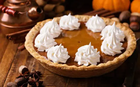 Pastel de calabaza decorado con crema batida, listo para los postres de Acción de Gracias. Especias y calabazas al fondo.