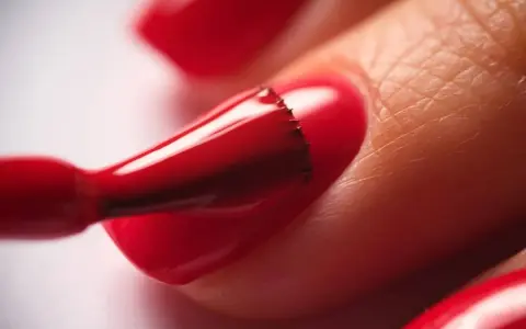 Application d'un vernis rouge vif sur un ongle. Le temps de séchage du vernis à ongles est crucial pour un fini parfait.