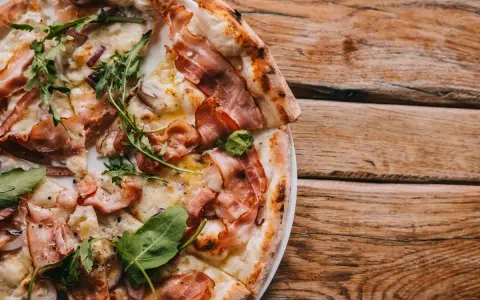 Pyszna pizza carbonara z chrupiącym boczkiem i rukolą na drewnianym stole.