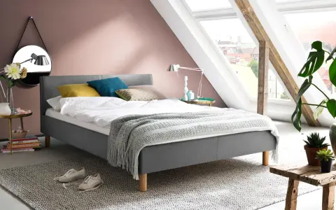 En mysig säng med kuddar i olika färger, en filt med fransar och en spegel på väggen. Frågan är hur litet får ett sovrum vara?