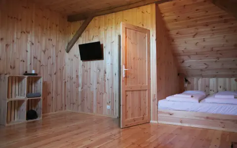 Przytulny stodoła domek z drewnianymi ścianami i podłogą. W pokoju łóżko, telewizor i regał z drewna.