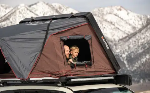 Vater und Kind schauen aus einem Dachzelt. Ein Abenteuer im Winter mit dem Dachzelt ist möglich.