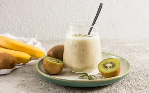 Un verre de smoothie banane kiwi, garni de graines de chia, avec des fruits frais autour.