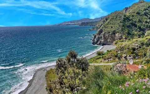 Ein malerischer granada strand mit felsigen Klippen, türkisfarbenem Meer und einer Stadt am Horizont.