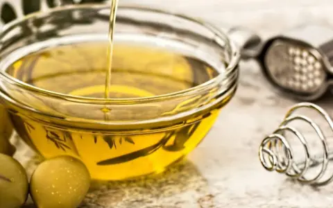 Aceite de oliva vertiéndose en un bol de cristal, rodeado de aceitunas. Varios tipos de aceite comestible para cocinar.
