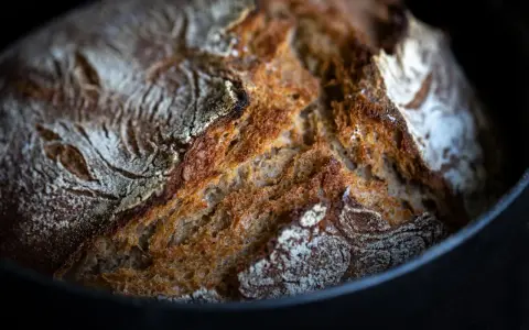 Frisch gebackenes Brot mit knuspriger Kruste ruht auf Backpapier im Gusseisentopf.
