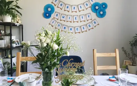 Urocze dekoracje na chrzest diy: girlanda "Chrzest Święty", bukiety białych kwiatów i ozdobne napisy.