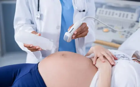 Badania prenatalne w 12 tygodniu ciąży: lekarz aplikuje żel na brzuch pacjentki przed badaniem USG.