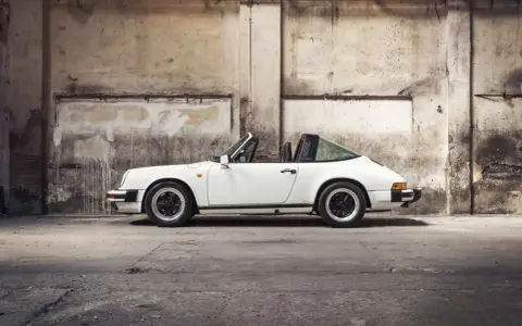 Weißer Porsche 911 3.2 Carrera Targa, ein Klassiker mit stabiler Wertentwicklung, steht in einer alten Lagerhalle.