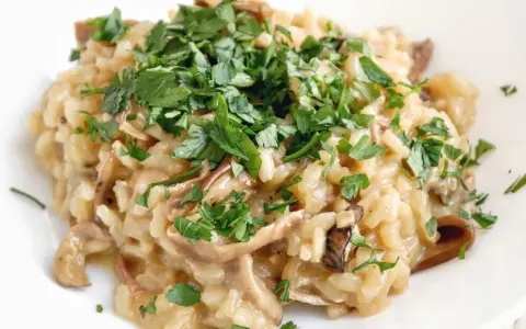 Kremowe risotto z grzybami, posypane świeżą natką pietruszki, wygląda apetycznie.