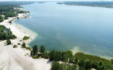 Plaża nad jeziorem, piasek, drzewa i ludzie odpoczywający w słońcu. Idealne miejsce na wakacje, jak z **pogoria** 1.