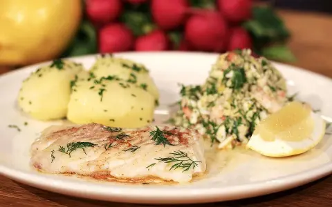 En tallrik med stekt kolja, dill, potatis och en citronskiva. Ett perfekt kolja recept för en god middag.