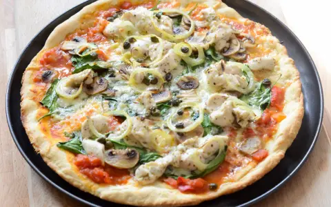 Pyszna pizza z kurczakiem, pieczarkami, szpinakiem i kaparami na cienkim cieście.