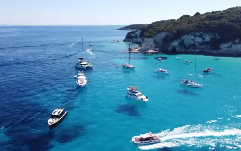 Båtar i turkost vatten vid en klippig kust, en idyllisk vy från Paxos, Grekland.