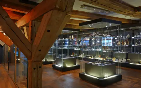 Wnętrze muzeum z zabytkowymi belkami i przeszklonymi gablotami pełnymi artefaktów. Może tu jest też błękitny baranek?