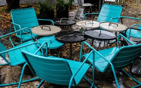 Teal metal chairs and tables, perfect for outdoor use, sit empty on a wet patio.
