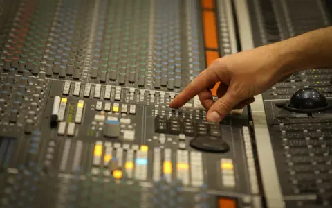 Main d'un ingénieur du son ajustant les faders d'une console de mixage, créant un son audio mono parfait.