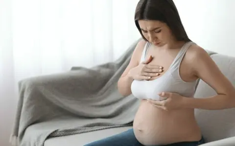 Ciężarna kobieta z bólem dotyka piersi, czując pierwsze oznaki siary.