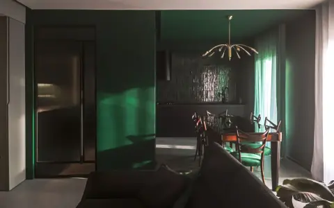 Un soggiorno moderno con pareti verde scuro, un divano antracite e una zona pranzo con sedie verdi. I colori da abbinare al verde scuro sono il legno scuro e l'ottone.