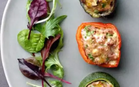Assiette de légumes farcis : poivron rouge, courgette et aubergine, garnis d'une préparation savoureuse, accompagnés d'une salade verte.