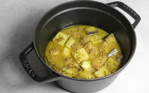 Un plat mijoté de colombo de porc avec des morceaux de pommes de terre et des épices dans une cocotte en fonte noire.