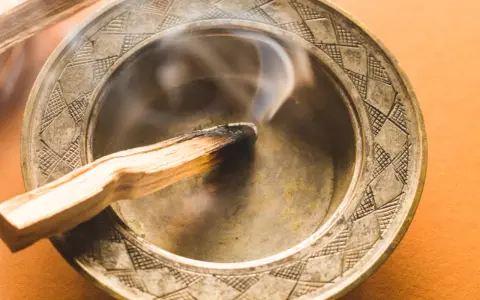 Humo ascendente de un palo santo quemándose en un cuenco metálico. Descubre a qué huele el palo santo.