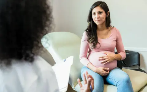 Schwangere Frau im Gespräch mit Arzt. Sie fragt sich, wie lange dauert eine einleitung, während sie ihren Bauch streichelt.