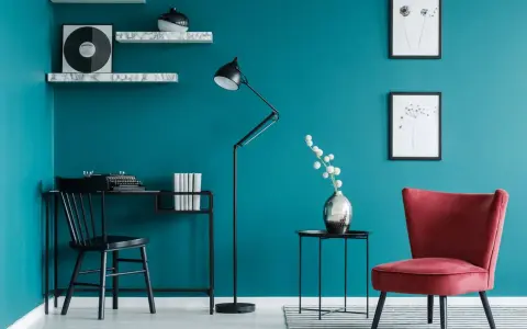 Bureau noir avec machine à écrire, lampe sur pied, fauteuil rouge et étagères sur un mur bleu ou vert canard.