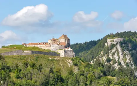 Fort de Joux, un site historique à visiter dans le Doubs, perché sur une colline verdoyante sous un ciel bleu.