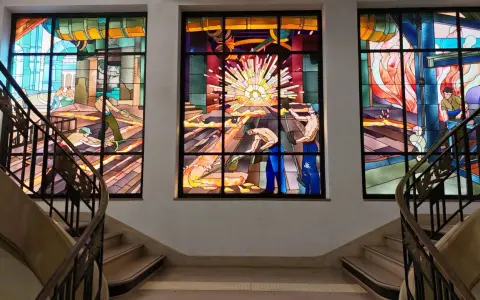 Vitraux Majorelle Longwy : trois verrières illustrant des scènes industrielles avec des ouvriers au travail, baignées de lumière.