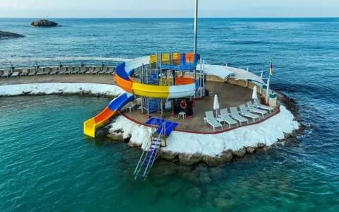 Kolorowe zjeżdżalnie wodne i leżaki na wyspie w Orange County Alanya, nad turkusowym morzem.