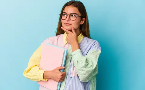 Młoda kobieta w okularach z zeszytami zastanawia się nad ciekawymi kierunkami studiów dla niezdecydowanych.