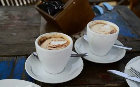 Zwei Tassen Kaffee Latte mit Milchschaum und Kakao-Muster auf einem Holztisch.