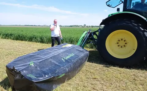Mężczyzna prezentuje nowoczesne kosiarki dyskowe SaMASZ obok zielonego traktora na polu.