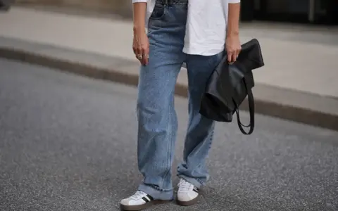 Modne jeansy flare w stylizacji z białą koszulą i czarną torebką.