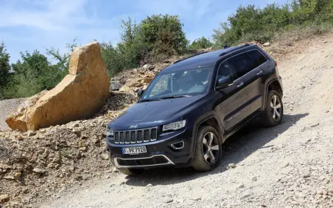Schwarzer Jeep Grand Cherokee 3.0 CRD 250 PS im Gelände. Ein großer Felsbrocken liegt daneben.
