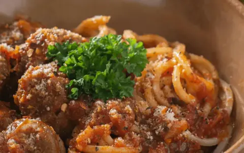 En skål med läckra polpette al sugo, köttbullar i tomatsås, serverade med pasta och toppade med färsk persilja och parmesan.