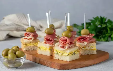 Eleganckie mini przekąski na imprezę: kanapki z szynką, jajkiem i oliwkami na wykałaczkach.