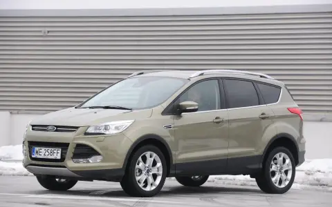 Złoty Ford Kuga 2.0 TDCI z polskimi tablicami WE 258FF zaparkowany na tle industrialnej ściany.